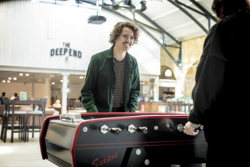 Male student playing foosball in the Deep end student bar