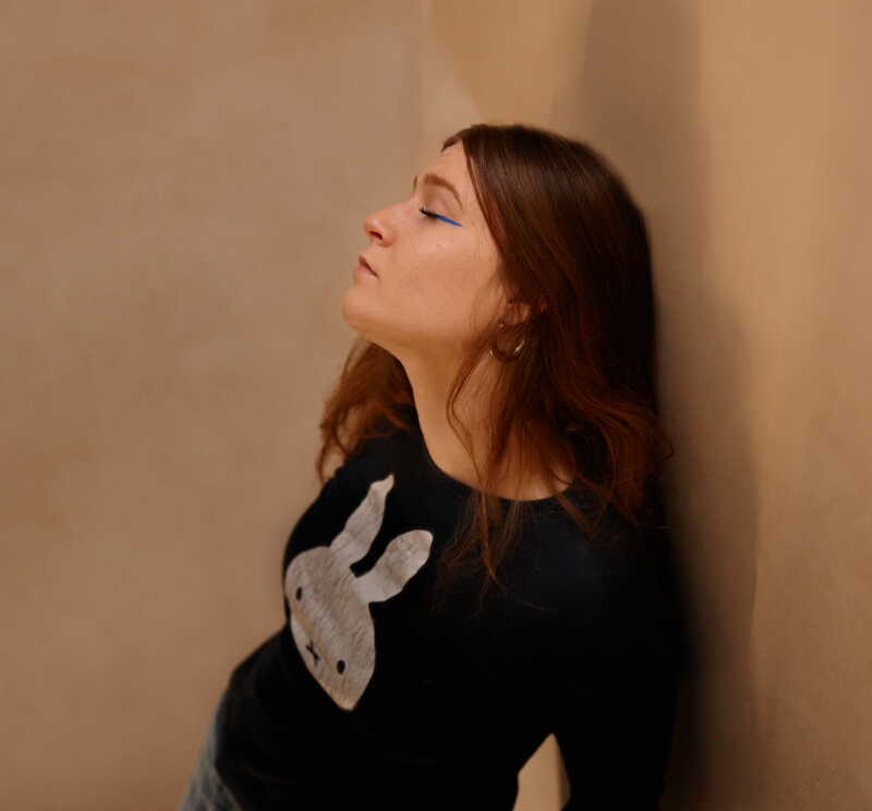 Young woman leaning against a wall, eyes closed in contemplation of the ineffable
