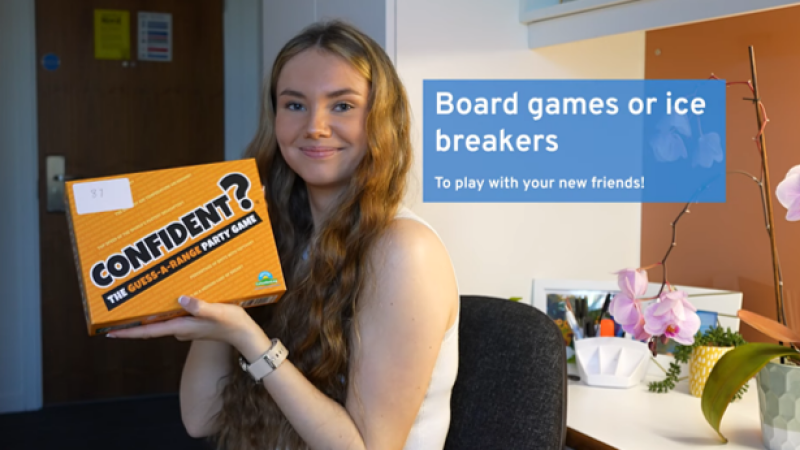 Female student smiling at camera holding a board game