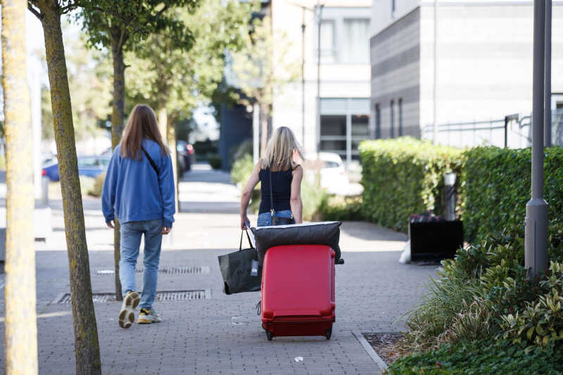 Female student wheeling suitcase to room
