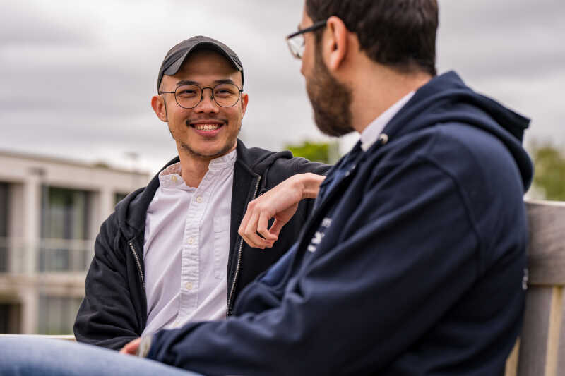 Two masters students chatting on bench on campus