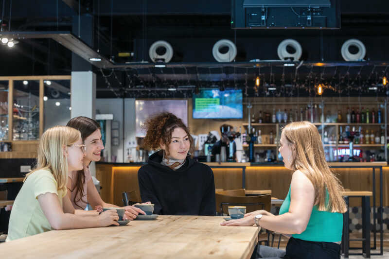 Three female students chatting with Kent Union student welfare officer in Woody's bar