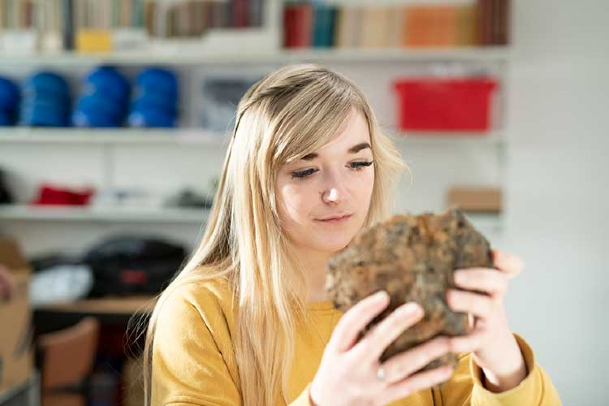 Student with long blonde hair holding a rock
