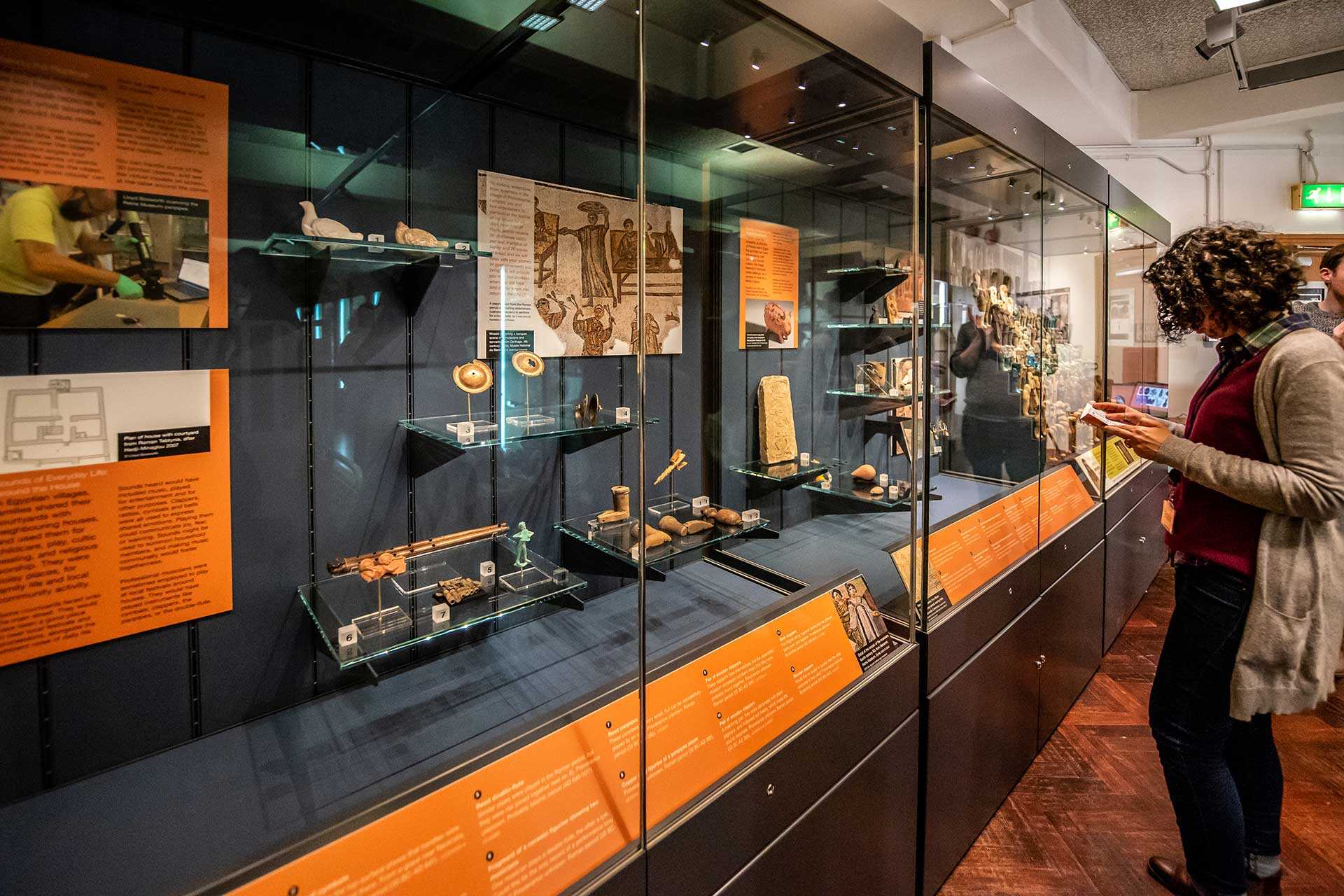 Various Roman and Late Antique artefacts in glass case with woman reading pamphlet in front of the case