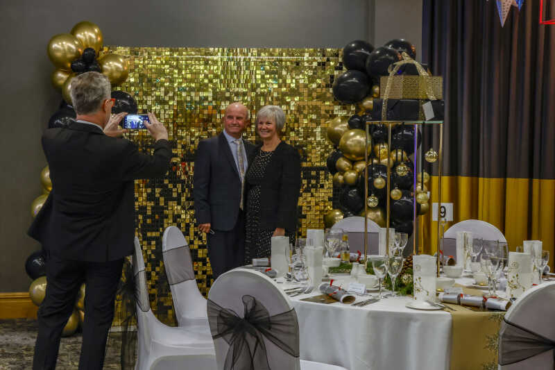 A couple having their photo taken in front of a gold, shinny photo wall