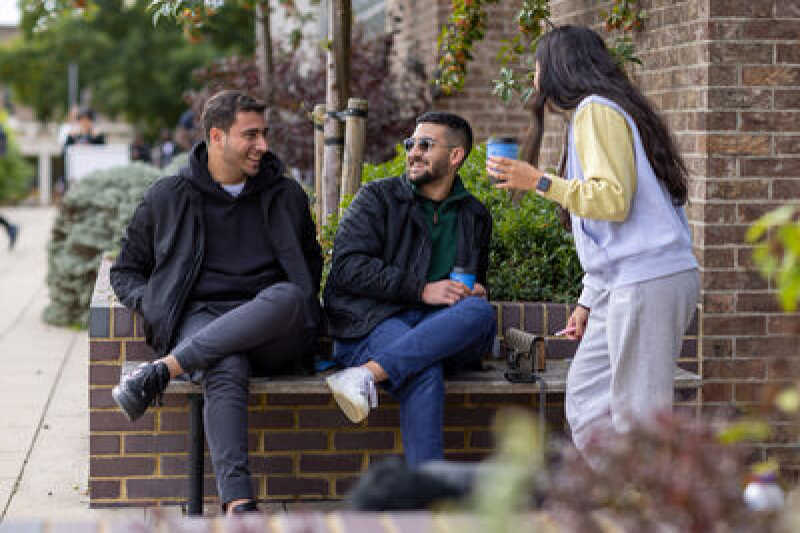 Three students sitting outside drinking coffee