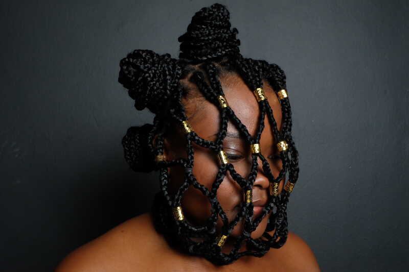 Image shows a young black woman with hair intricately braided across her face