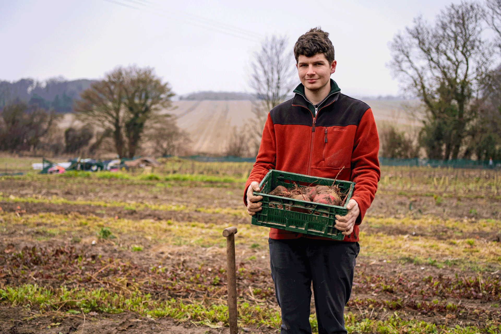 Student Jack on his farm holding basket of vegetables he has grown.