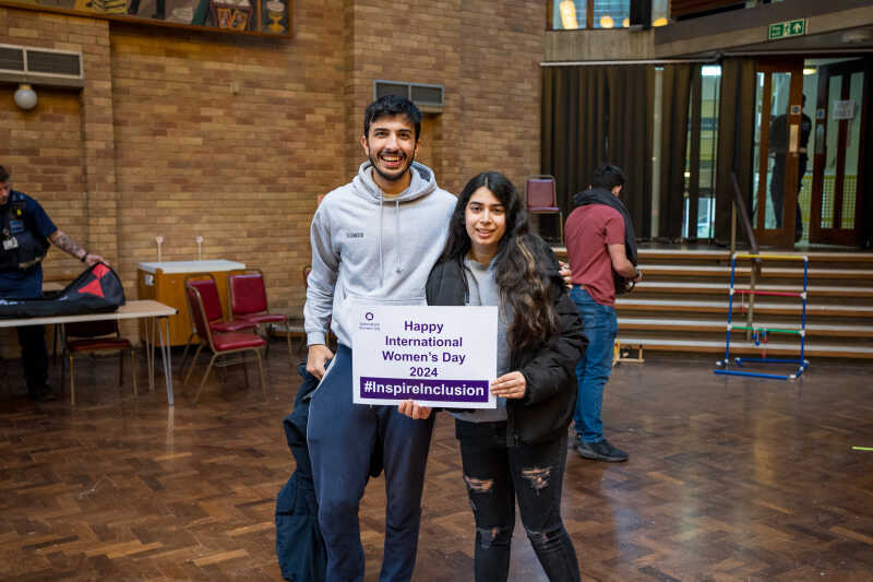 Two students in the Rutherford Dining Hall  holding up International Women's Day pledge cards