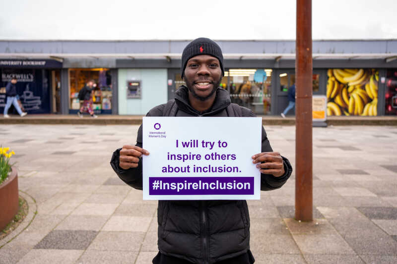 A student outside smiling and holding up International Women's Day pledge card