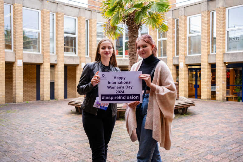 Two students outside smiling and holding up International Women's Day pledge card