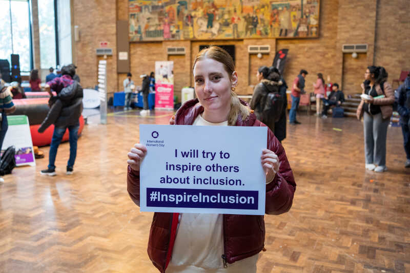 A student in the Rutherford Dining Hall holding up an International Women's Day pledge card