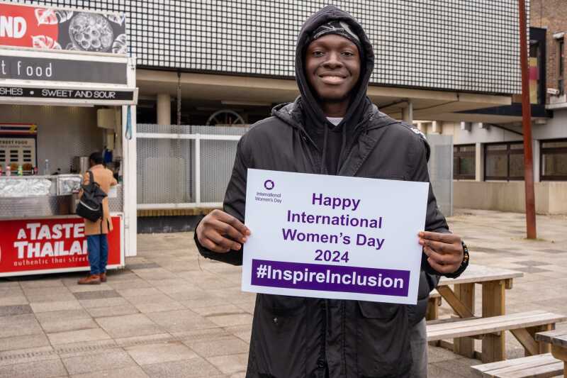 A student outside on campus holding up an International Women's Day pledge card