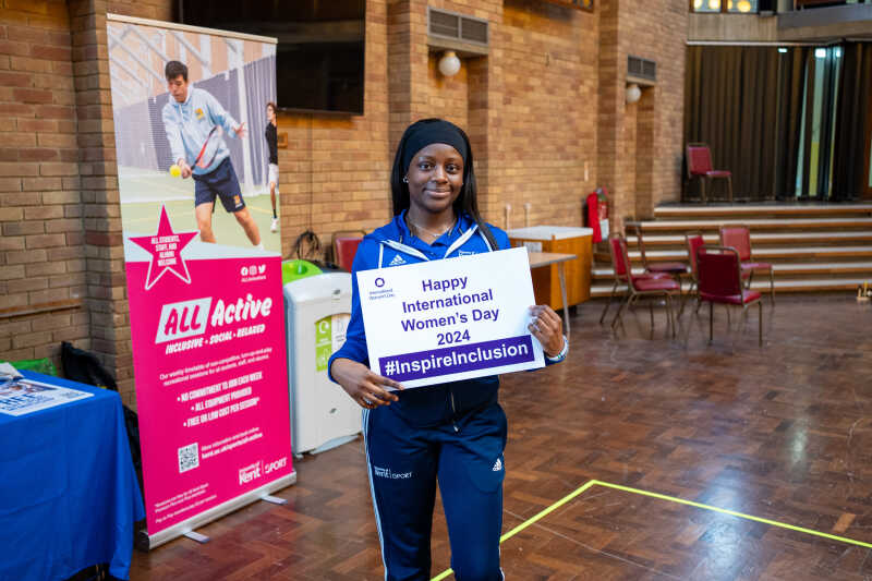 A Kent Sport staff member in the Rutherford Dining Hall holding up an International Women's Day pledge card