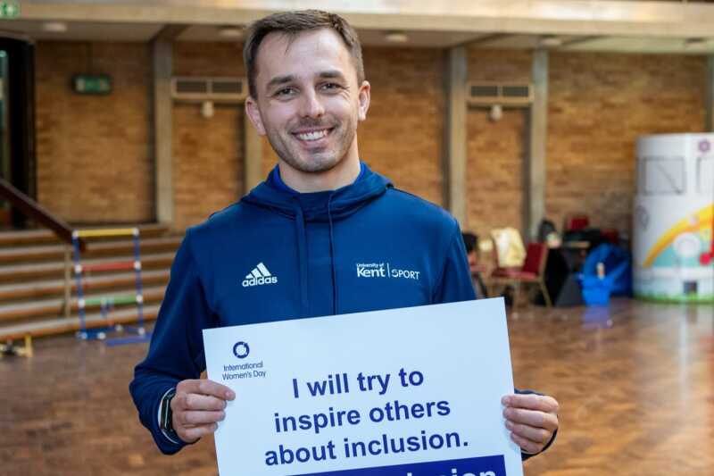 A Kent Sport staff member in the Rutherford Dining Hall holding up an International Women's Day pledge card