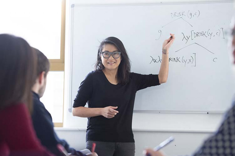 Christina Kim, black hair, glasses, black jumper teaching at a whiteboard