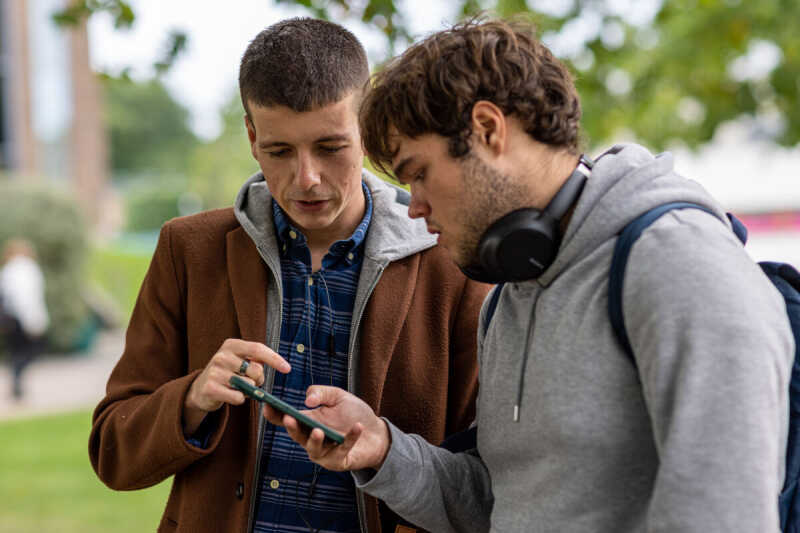 Image shows two men, one wearing headphones, pointing to information on a phone