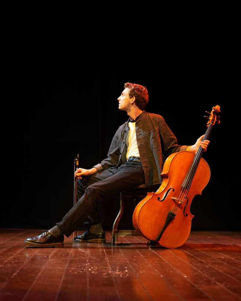 Male cellist sitting sideways to camera looking off to his right