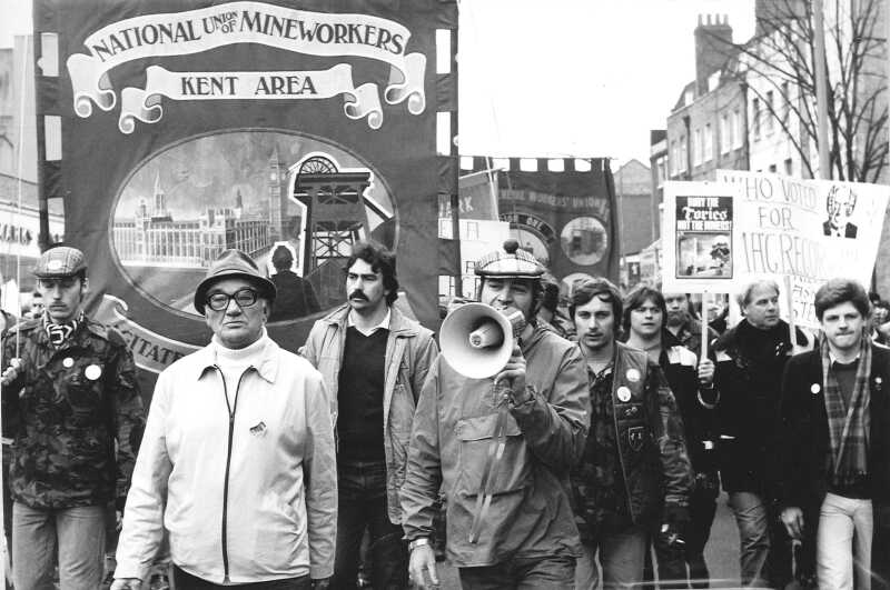 Balck and white photograph of a crowd of miner's and their supporters, carrying an NUM Kent Area banner