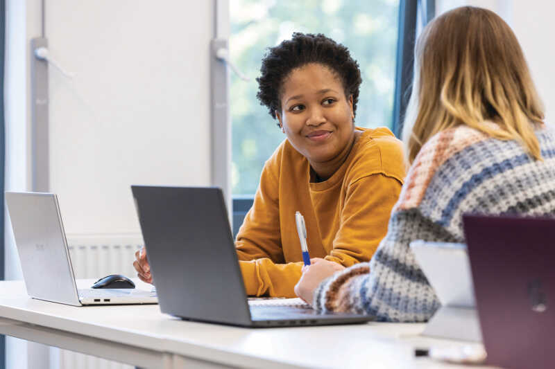 Two people talking and looking at laptops