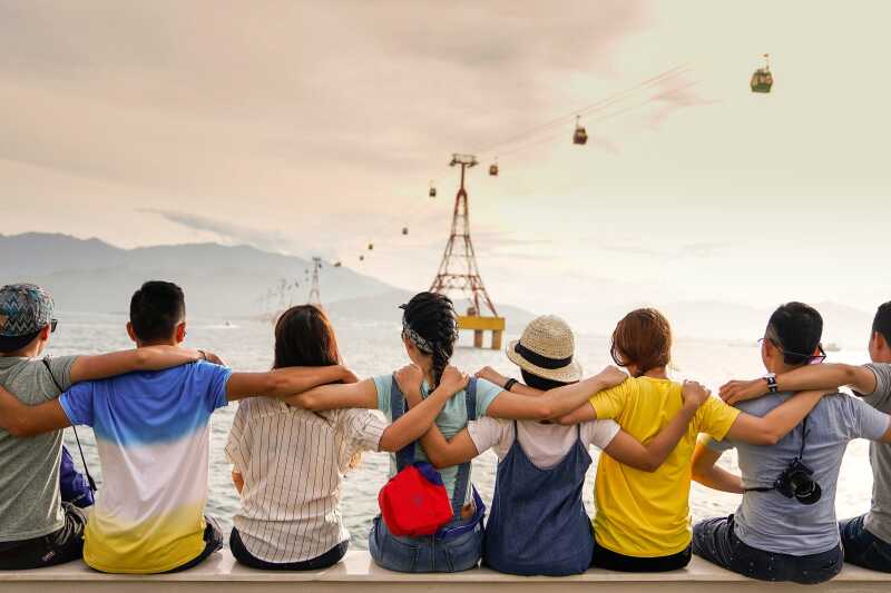 young people sitting in a row on a ledge looking out to the sea and embracing one another