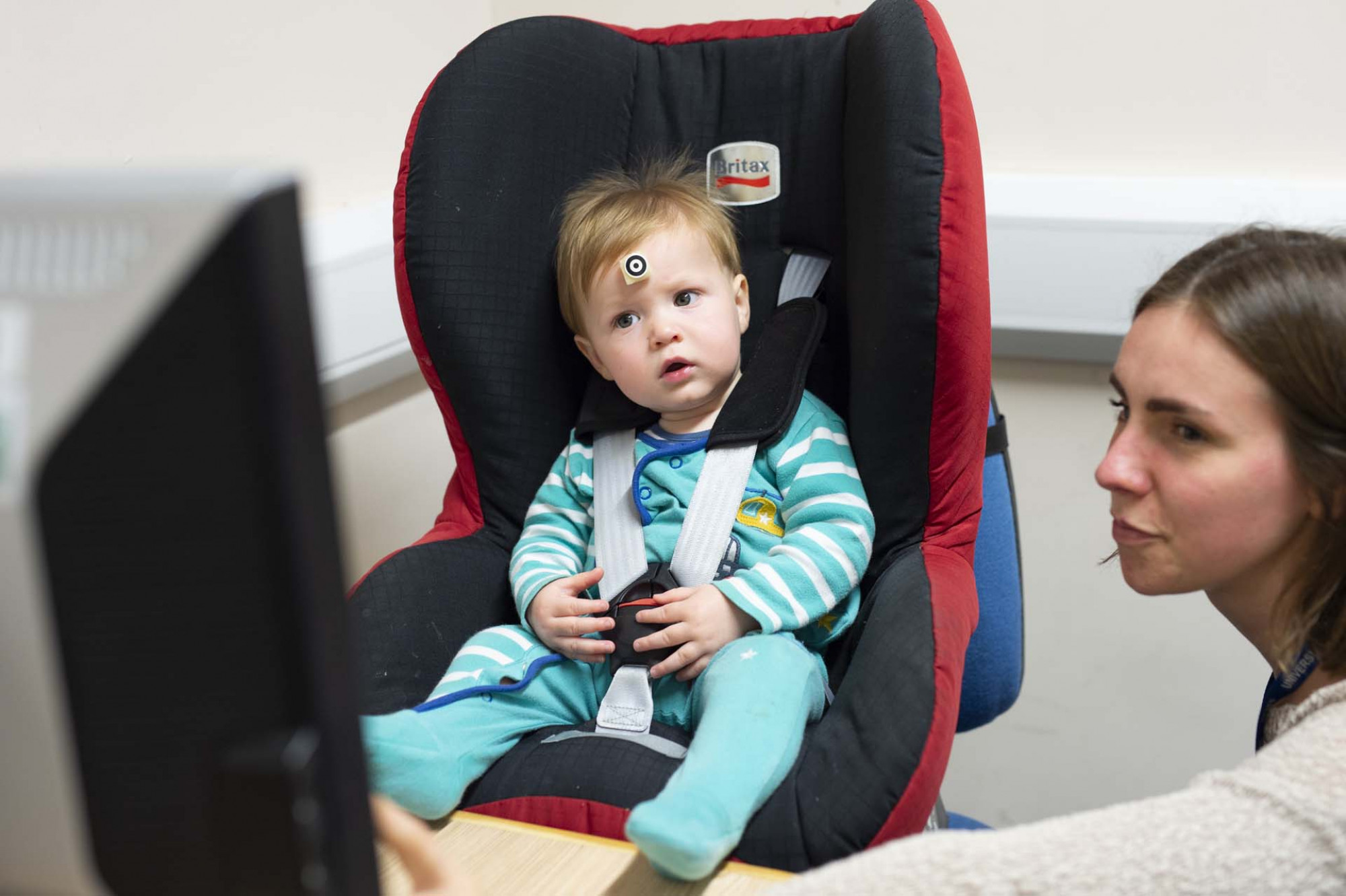 Young child in seat and in front of screen with psychologist alongside