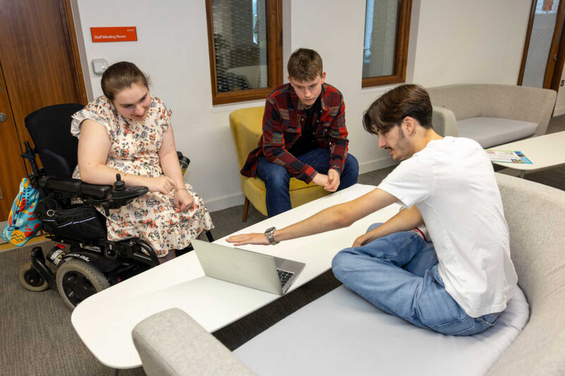 Image shows a group of people sat of sofas and talking