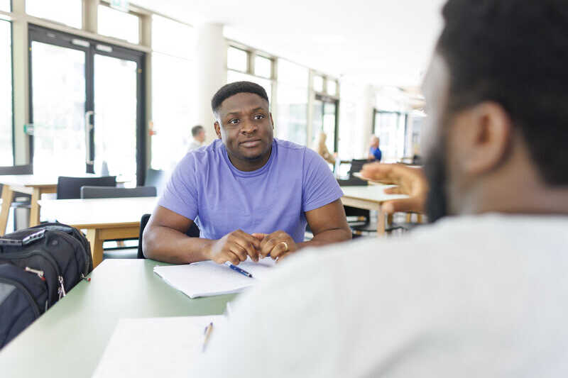 Student sat at a table talking to another student