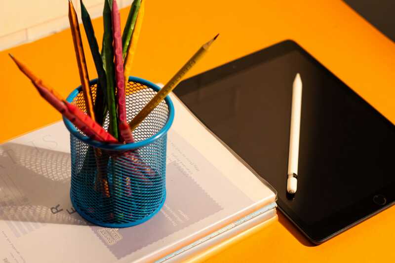 a picture of a pencil holder with pencils of different colours next to a tablet