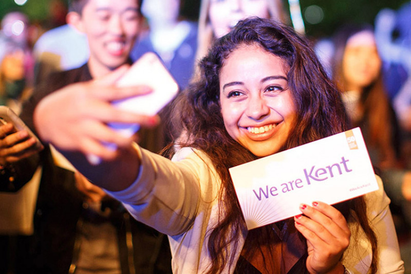 Smiling female students takes selfie while holding We are Kent placard