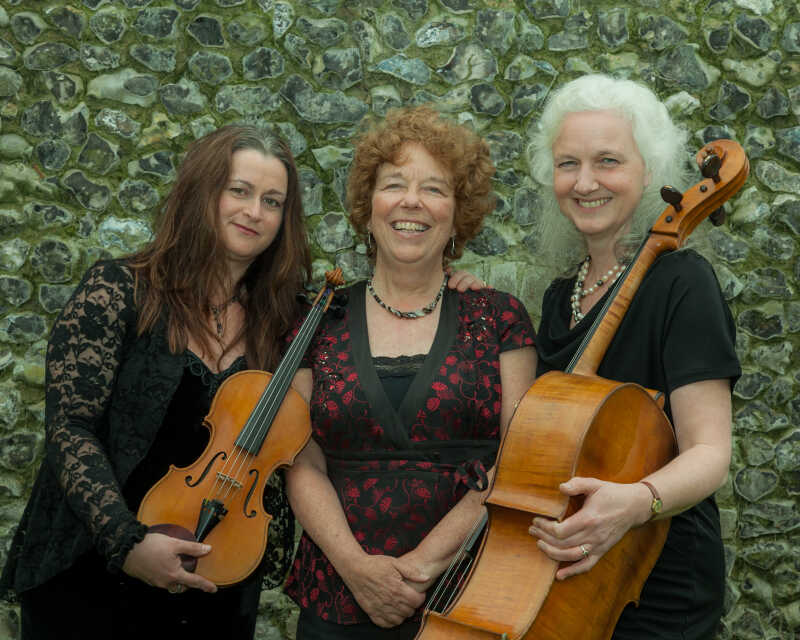Three female musicians standing in front of a knapped flint wall