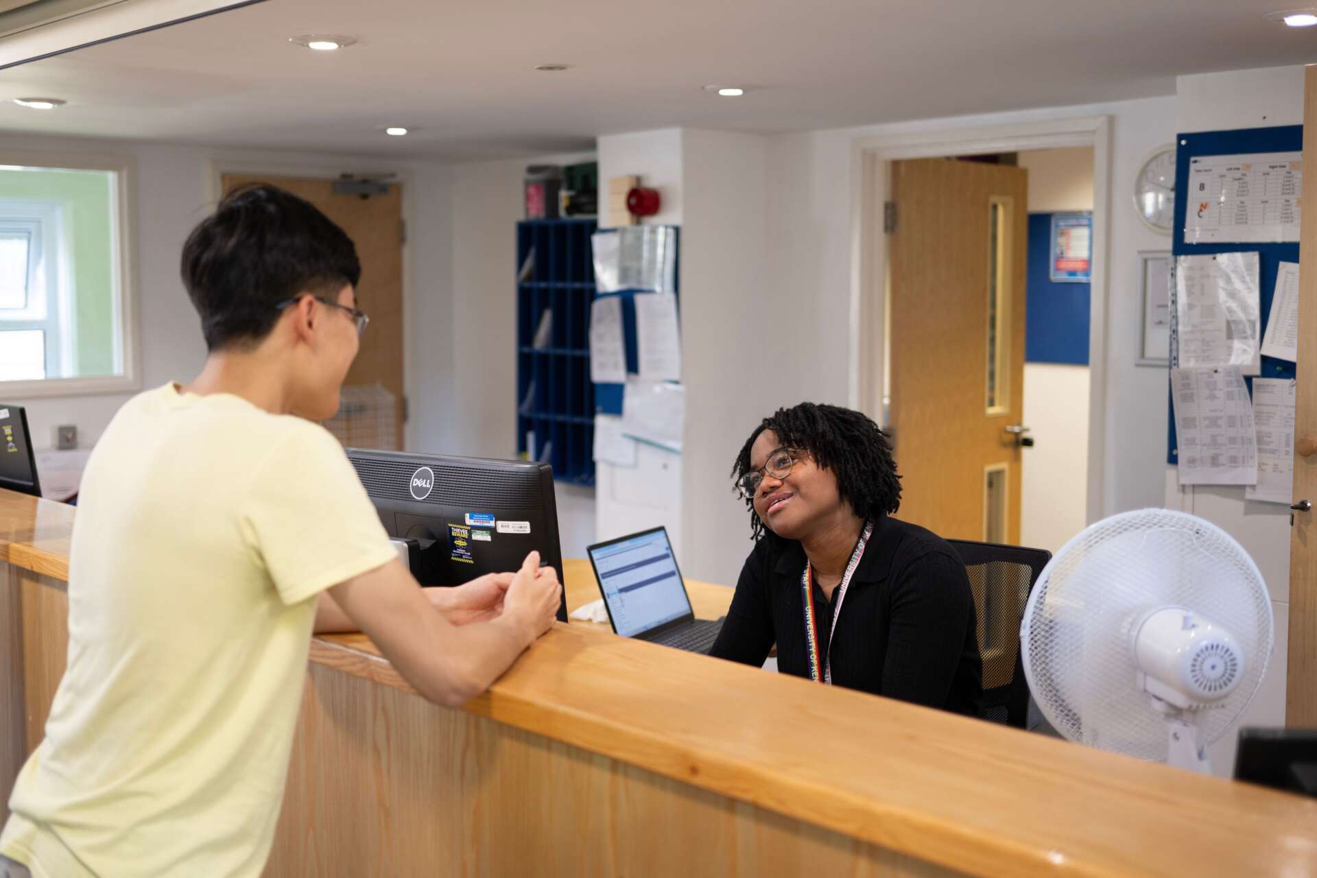 A student leaning on the reception counter, talking to a female receptionist