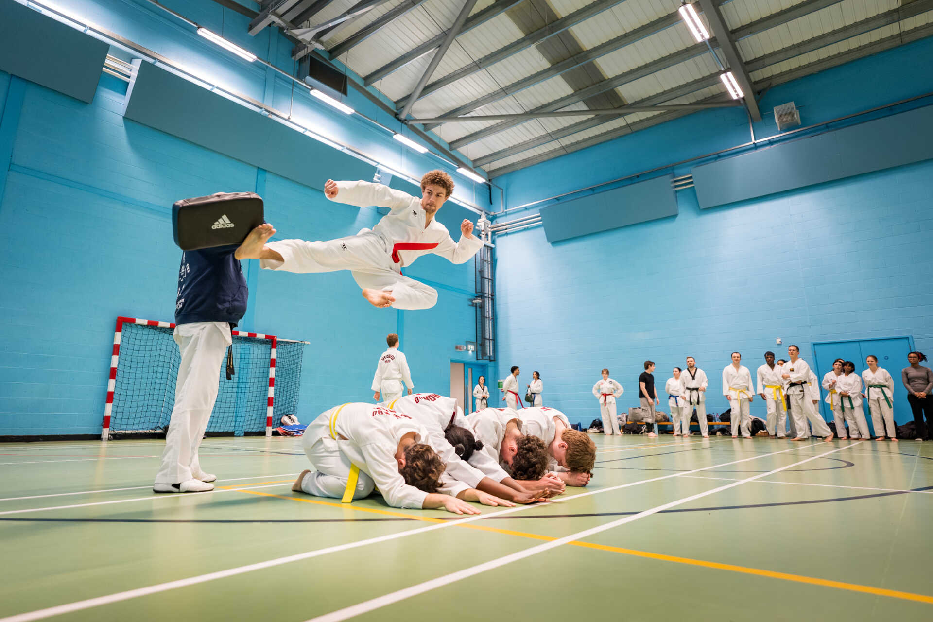 Student Angus doing flying side kick over multiple people