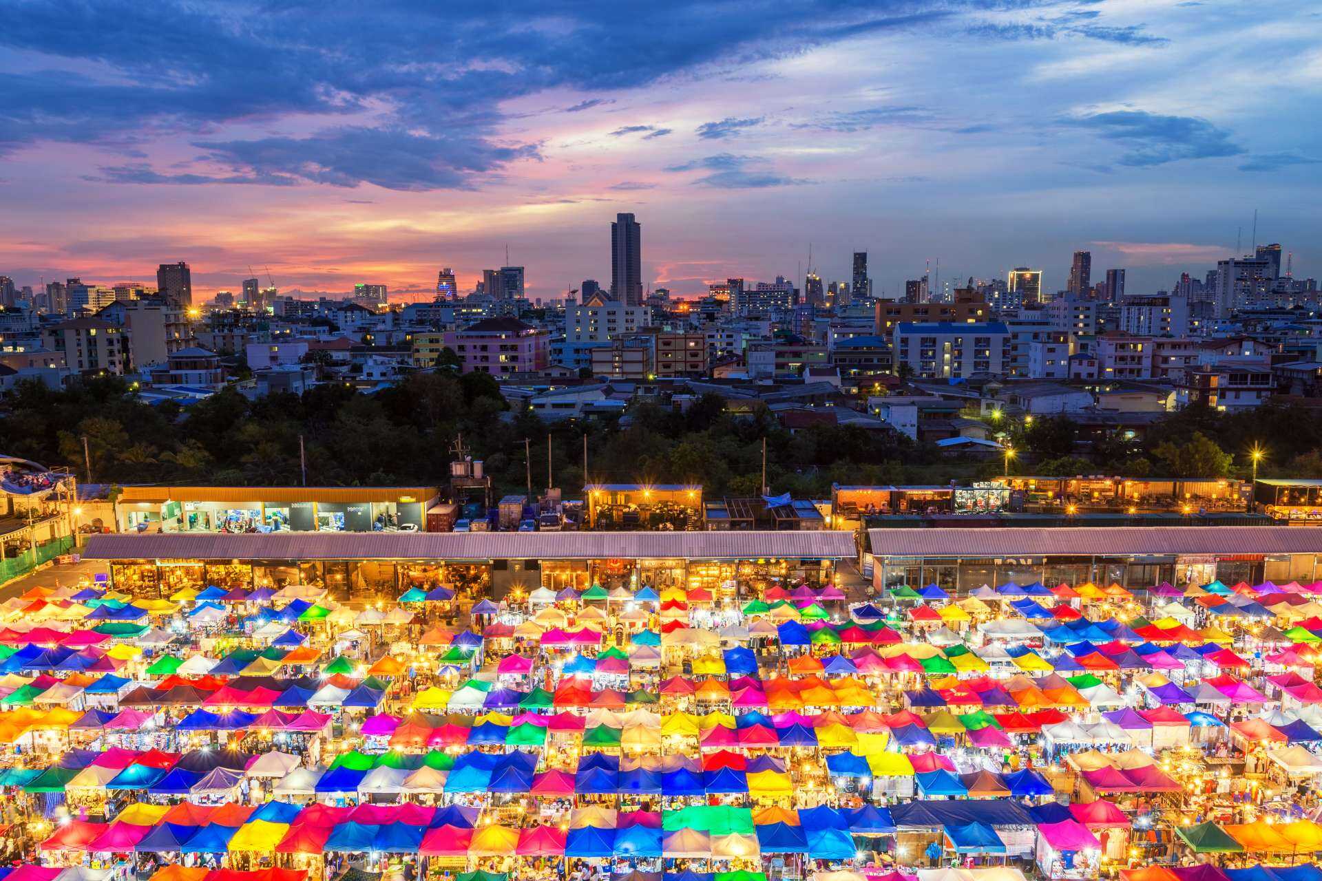 Panoramic view of a large colourful market in Bangkok with apartments and skyscrapers in the background