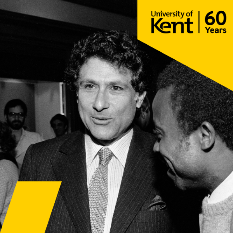 black and white photo of middle aged white man speaking and smiling with a black man in the foreground turned towards him