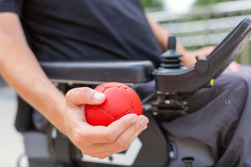 Close-up photo of someone in a wheelchair holding a ball in their hand, ready to play boccia