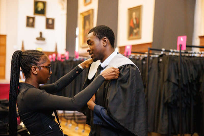 student being assisted with his gown