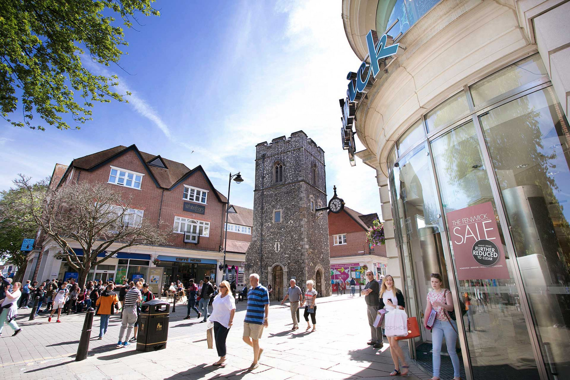 People walking along the busy Canterbury high street past the historical clock tower