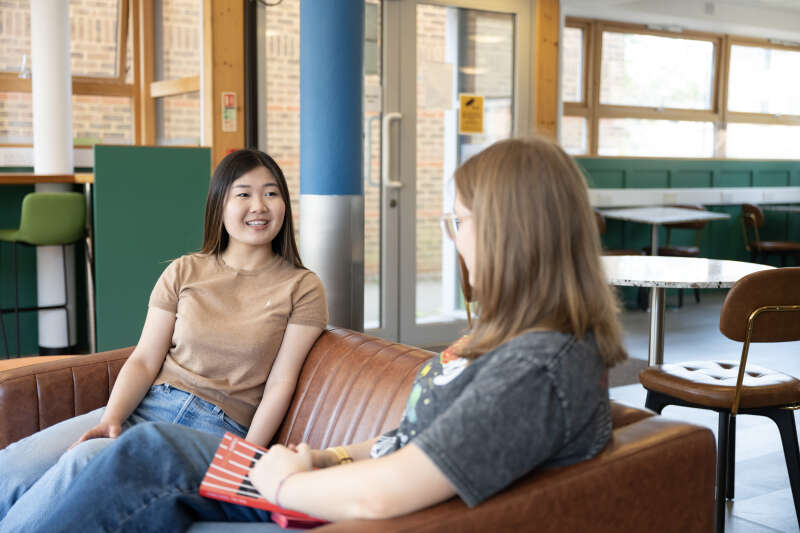 Two female students sitting on a sofa chatting.