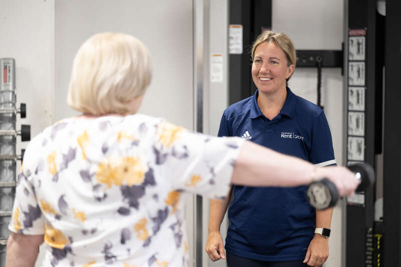 Exercise Referral client looking at a member of staff while raising a weight with their right arm.