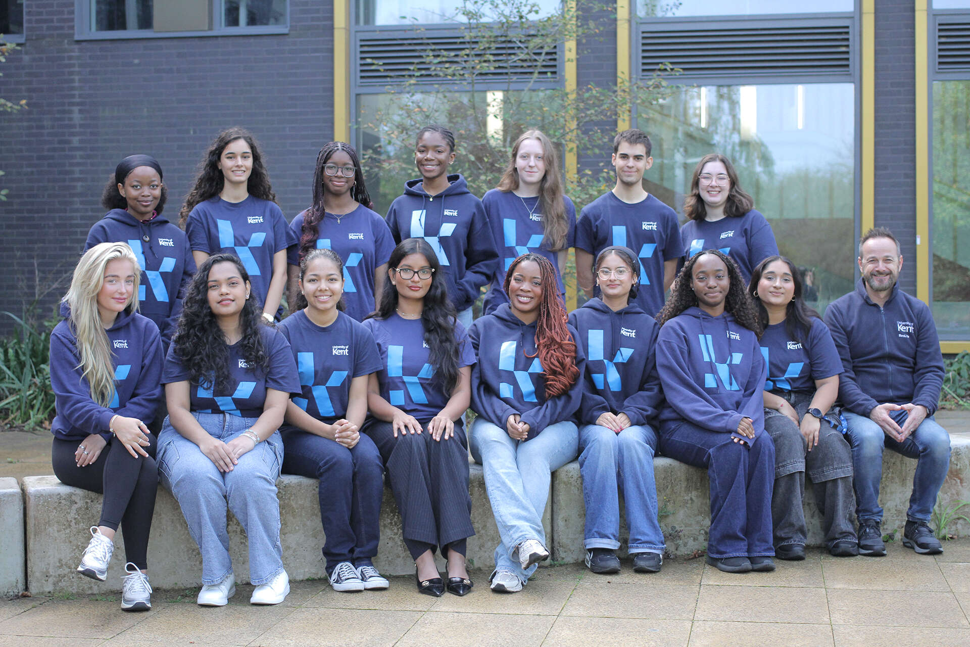 University of Kent ResLife team posing outdoors in front of campus building, wearing navy Kent-branded shirts and hoodies.