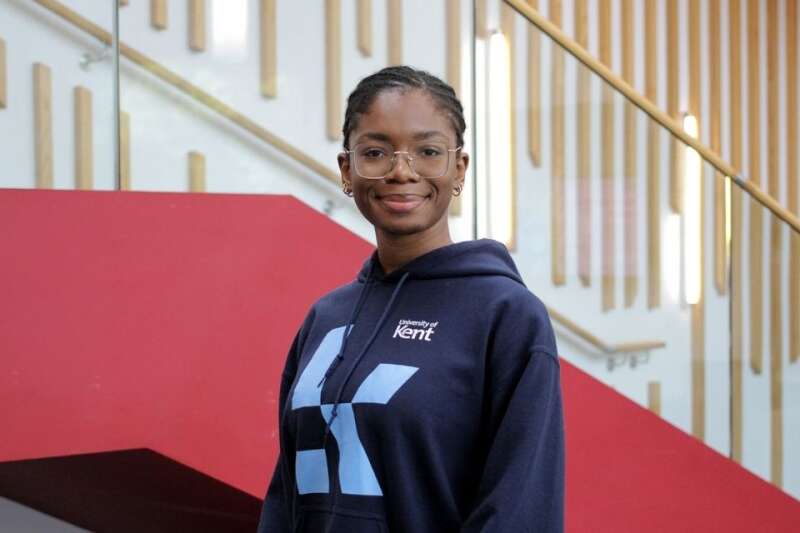 Deni in a blue Kent branded hoodie, posing by the stairs in our Kennedy building.