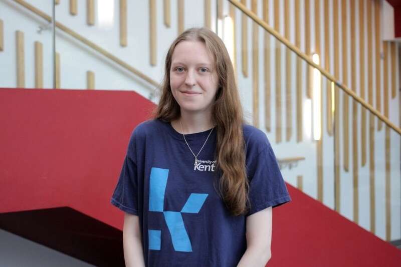 Isabel in a blue Kent branded t-shirt, posing by the stairs in our Kennedy building.