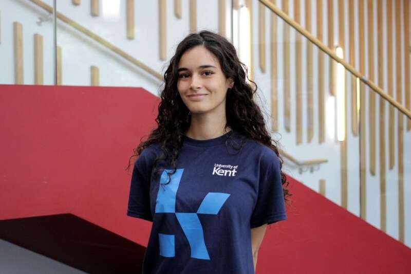 India in a blue Kent branded t-shirt, posing by the stairs in our Kennedy building.
