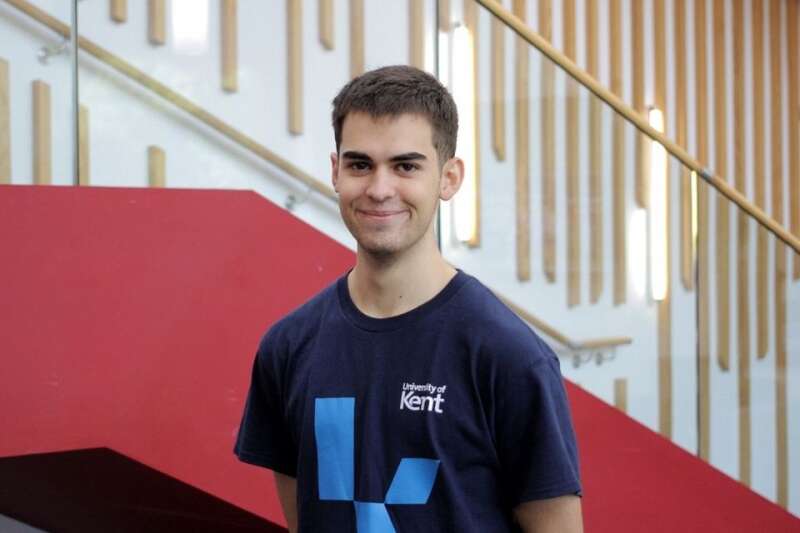 Evan in a blue Kent branded t-shirt, posing by the stairs in our Kennedy building.