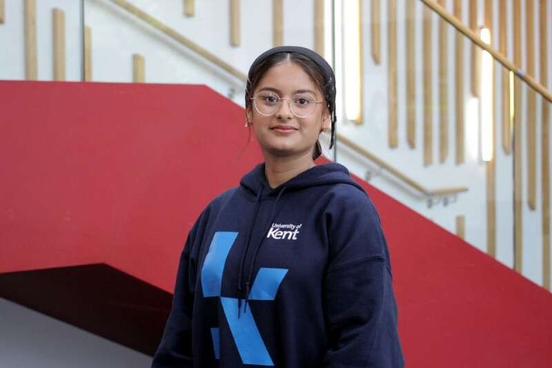 Attia in a blue Kent branded hoodie, posing by the stairs in our Kennedy building.