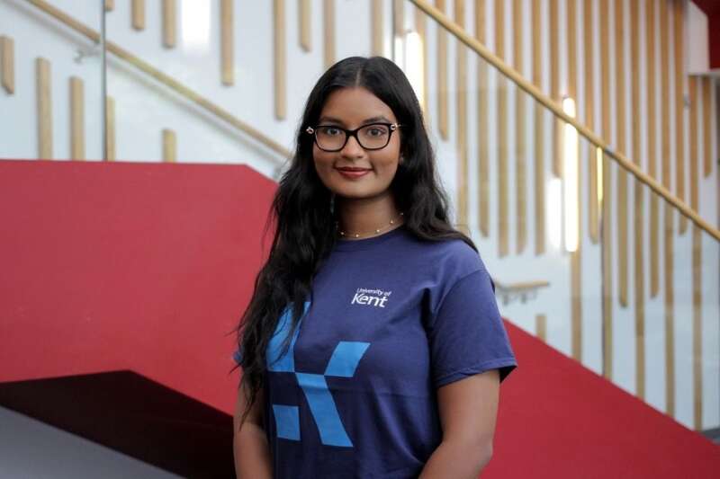 Tehara in a blue Kent branded t-shirt, posing by the stairs in our Kennedy building.