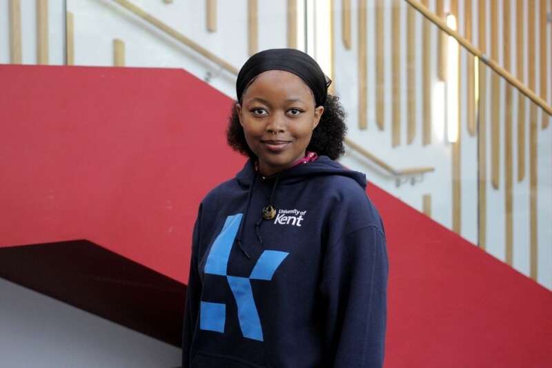 Panashe in a blue Kent branded hoodie, posing by the stairs in our Kennedy building.