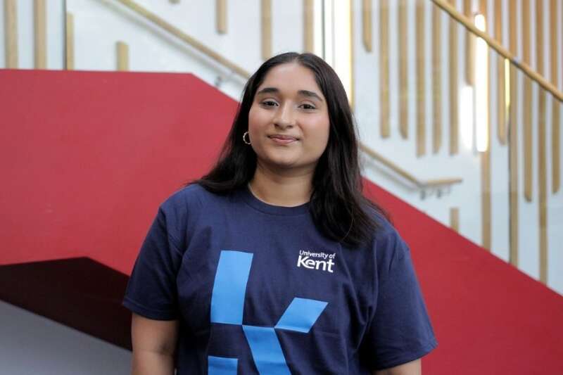 Freny in a blue Kent branded t-shirt, posing by the stairs in our Kennedy building.