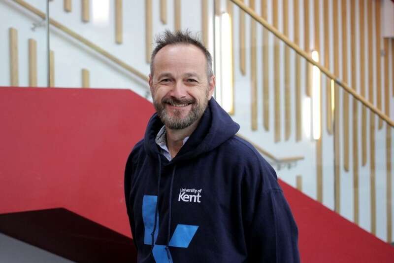 Ewen in a blue Kent branded hoodie, posing by the stairs in our Kennedy building.
